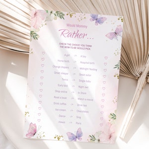 Puede incluir: Un juego de baby shower rosa y dorado con el texto "Would Mommy Rather..." y una lista de preguntas para que los invitados adivinen las preferencias de la futura mam&aacute;. El juego presenta un dise&ntilde;o floral con mariposas.