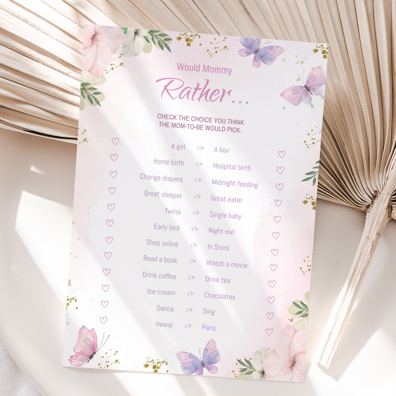 Puede incluir: Un juego de baby shower rosa y dorado con el texto "Would Mommy Rather..." y una lista de preguntas para que los invitados adivinen las preferencias de la futura mam&aacute;. El juego presenta un dise&ntilde;o floral con mariposas.