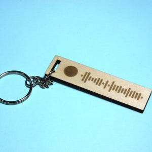 Peut inclure: Un porte-cl&eacute;s en bois avec un code Spotify grav&eacute; dessus. Le porte-cl&eacute;s est attach&eacute; &agrave; un anneau de cl&eacute; argent&eacute;.