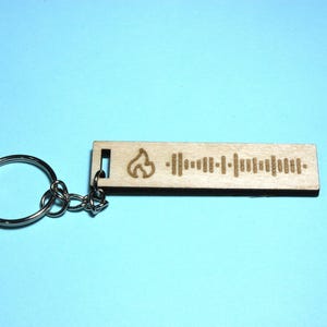 Peut inclure: Un porte-cl&eacute;s en bois avec un motif de flamme et un code Spotify. Le porte-cl&eacute;s est attach&eacute; &agrave; un anneau de cl&eacute; argent&eacute;.