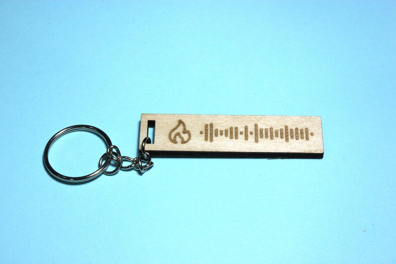 Peut inclure: Un porte-cl&eacute;s en bois avec un motif de flamme et un code Spotify. Le porte-cl&eacute;s est attach&eacute; &agrave; un anneau de cl&eacute; argent&eacute;.