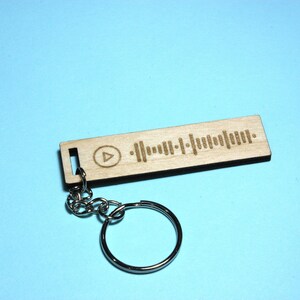 Peut inclure: Un porte-cl&eacute;s en bois avec un code Spotify grav&eacute; au laser et un bouton de lecture. Le porte-cl&eacute;s est attach&eacute; &agrave; un anneau de cl&eacute; en m&eacute;tal argent&eacute;.