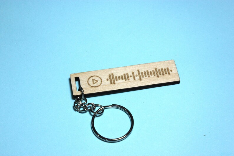 Peut inclure: Un porte-cl&eacute;s en bois avec un code Spotify grav&eacute; au laser et un bouton de lecture. Le porte-cl&eacute;s est attach&eacute; &agrave; un anneau de cl&eacute; en m&eacute;tal argent&eacute;.