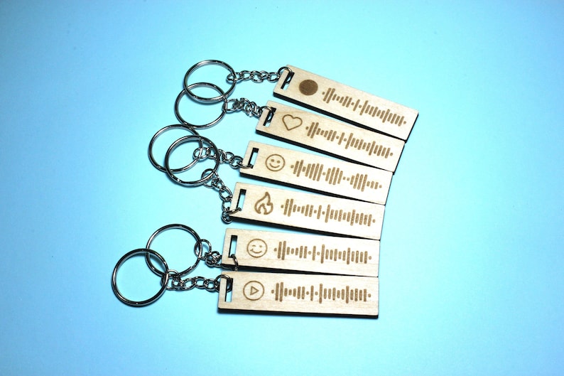Peut inclure: Ensemble de sept porte-cl&eacute;s en bois avec diff&eacute;rents symboles et codes Spotify grav&eacute;s dessus. Les symboles comprennent un cercle, un c&oelig;ur, un visage souriant, une flamme, un autre visage souriant et un bouton de lecture. Chaque porte-cl&eacute;s est attach&eacute; &agrave; un anneau de cl&eacute; argent&eacute;.