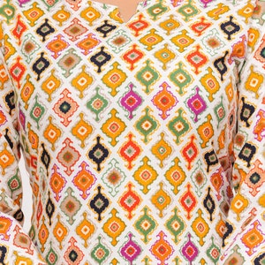 K&ouml;nnte beinhalten: Wei&szlig;es Langarm-Oberteil mit einem farbenfrohen geometrischen Muster. Das Muster zeigt Rauten in Orange, Gelb, Gr&uuml;n, Pink und Marineblau. Das Oberteil hat einen geschlitzten Ausschnitt und eine lockere Passform.