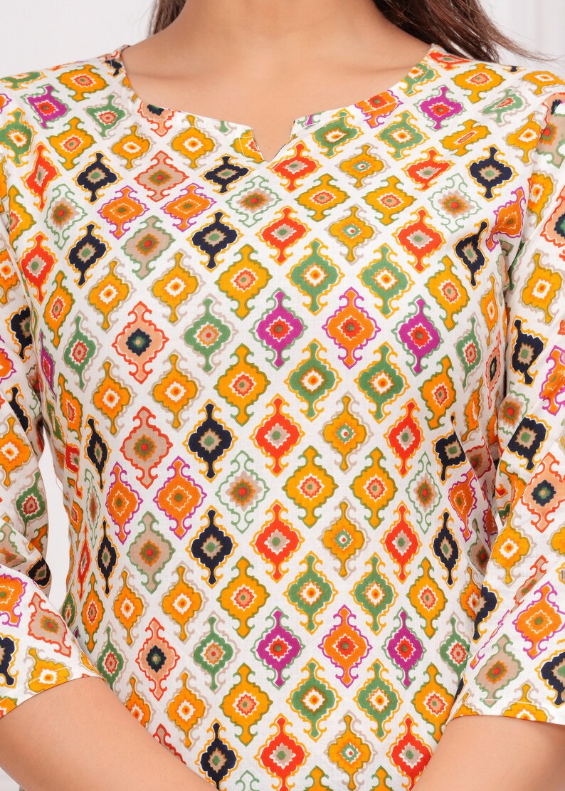 K&ouml;nnte beinhalten: Wei&szlig;es Langarm-Oberteil mit einem farbenfrohen geometrischen Muster. Das Muster zeigt Rauten in Orange, Gelb, Gr&uuml;n, Pink und Marineblau. Das Oberteil hat einen geschlitzten Ausschnitt und eine lockere Passform.