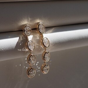 May include: A pair of gold earrings with five oval-shaped clear gemstones hanging from each earring.