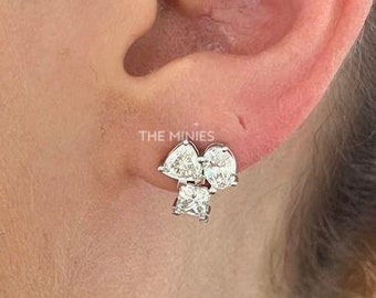 May include: Close-up of a person's ear wearing a pair of silver earrings with small, clear cubic zirconia stones. The earrings are shaped like a cluster of three stones, with two triangular stones and one round stone.