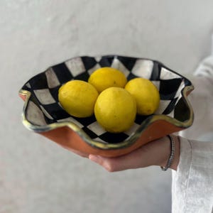 以下が含まれることがあります： 内側が白黒の市松模様、外側がテラコッタ色の装飾用セラミックボウル。 ボウルには4つの明るい黄色のレモンが入っています。縁は金色の塗料でトリミングされており、デザインにエレガンスを添えています。
