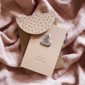 May include: A brown card with the text "love you lots and lots" and a silver heart charm with the text "love you" on a pink fabric background.