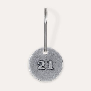 May include: A silver key chain with a round tag that has the number 21 embossed on it.