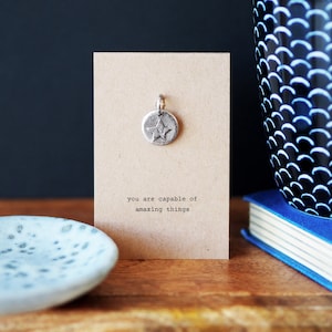 Peut inclure: Une carte en papier kraft avec un charme d'étoile argenté attaché. La carte indique "Vous êtes capable de choses incroyables."