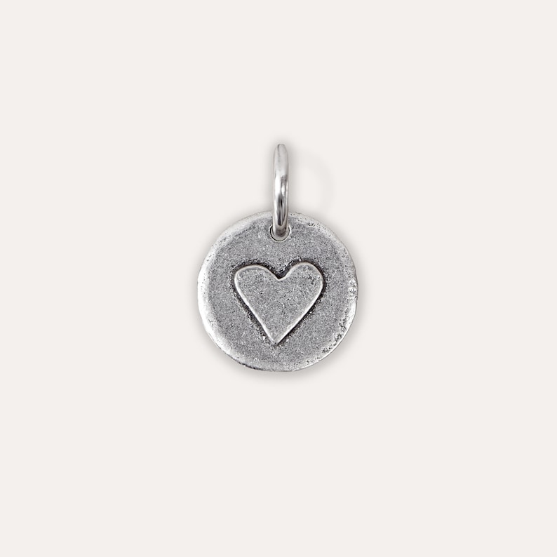 Peut inclure: Un charme en argent en forme de cercle avec un c&oelig;ur en relief au centre.