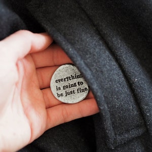 May include: A silver-toned round token with the words "everything is going to be just fine" engraved on it.