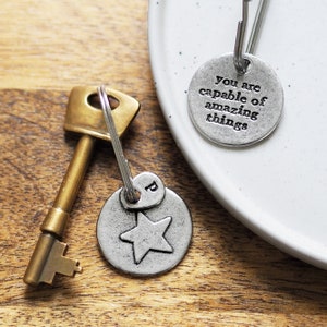 Può includere: Un portachiavi in ​​argento con un ciondolo a forma di stella e un'etichetta rotonda che dice "Sei capace di cose incredibili".