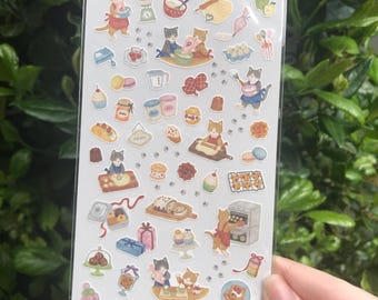 Op de afbeelding: Een vel stickers met schattige katten die in een keuken bakken. De stickers zijn op een witte achtergrond met een roze rand. De tekst "Little Kitchen" en "猫まみれさん" staat bovenaan het vel.