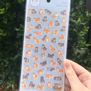 Puede incluir: Una hoja de pegatinas con adorables cachorros Shiba Inu en varias poses. Las pegatinas están sobre un fondo azul claro con el texto "まめまめ おにーちゃん sticker" y "マイバッグ マチ付きテープ付き" en japonés.