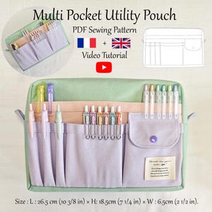 Op de afbeelding: Een multi-pocket utility pouch in lichtgroen en lavendel, gevuld met pennen en potloden. De pouch heeft meerdere compartimenten en een knoopsluiting. De afbeelding bevat de tekst "Multi Pocket Utility Pouch" en afmetingen van 26,5 cm L x 18,5 cm H x 6,5 cm B.