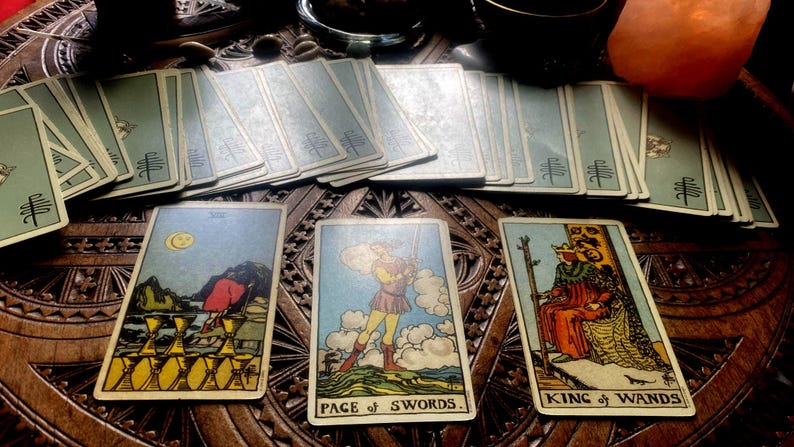 May include: A collection of tarot cards, featuring illustrations and titles like "Page of Swords" and "King of Wands." The cards are arranged on a carved wooden surface, with several decks visible. The color palette includes blues, yellows, and reds.