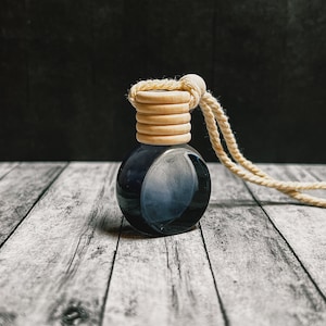 K&ouml;nnte beinhalten: Kleine, runde, dunkelblaue Glasflasche mit Holzverschluss und beigem Seil. Die Flasche hat einen Farbverlauf, der von Dunkelblau zu einem helleren Farbton &uuml;bergeht. Der Holzverschluss besteht aus mehreren gestapelten Ringen.