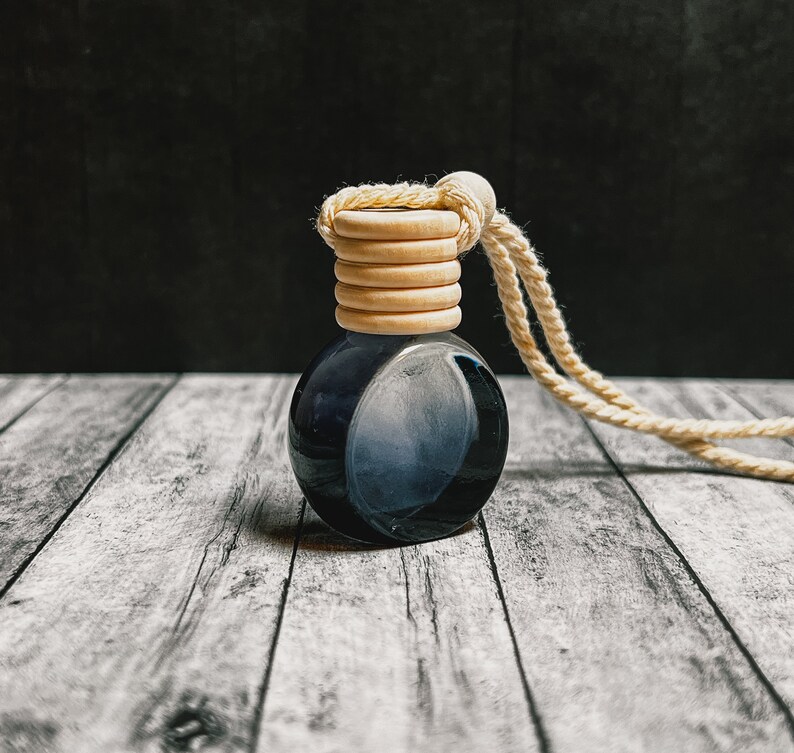 K&ouml;nnte beinhalten: Kleine, runde, dunkelblaue Glasflasche mit Holzverschluss und beigem Seil. Die Flasche hat einen Farbverlauf, der von Dunkelblau zu einem helleren Farbton &uuml;bergeht. Der Holzverschluss besteht aus mehreren gestapelten Ringen.