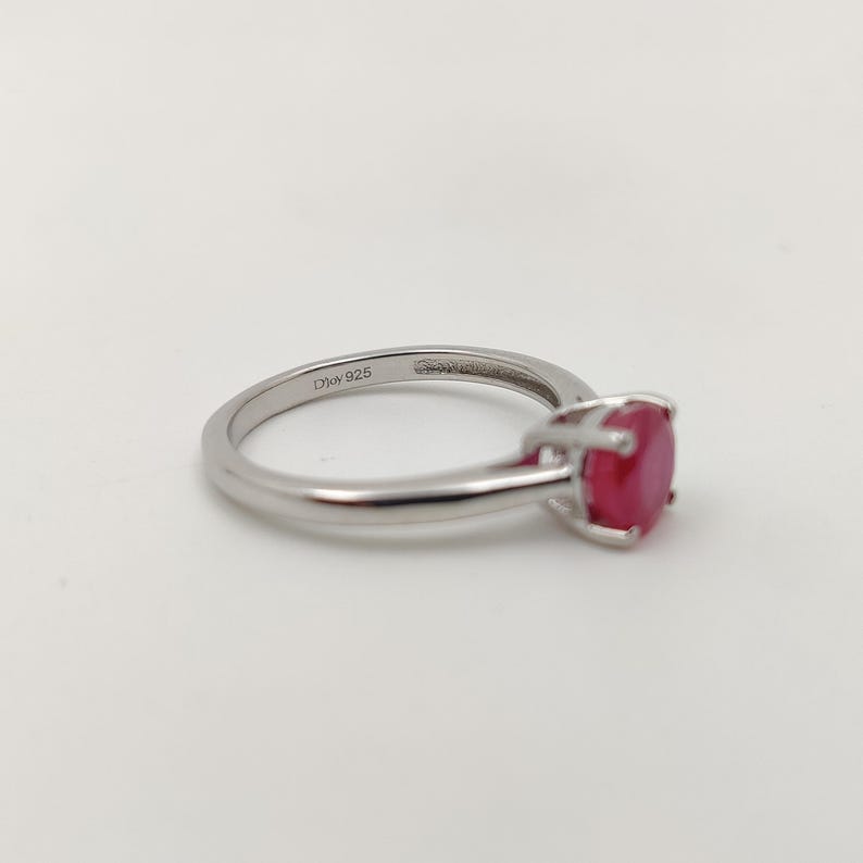 Puede incluir: Un anillo de plata con una gema roja grande, de corte ovalado. La banda del anillo es delgada y pulida, con la inscripci&oacute;n "Djoy 925". La gema roja es el punto focal, engastada en un engaste cl&aacute;sico de cuatro puntas.