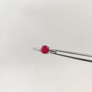 Puede incluir: Un anillo de plata con una gema roja vibrante y redonda. El anillo tiene una banda delgada y delicada, con la gema sujeta por cuatro peque&ntilde;as garras. El anillo se muestra sobre un fondo blanco liso.