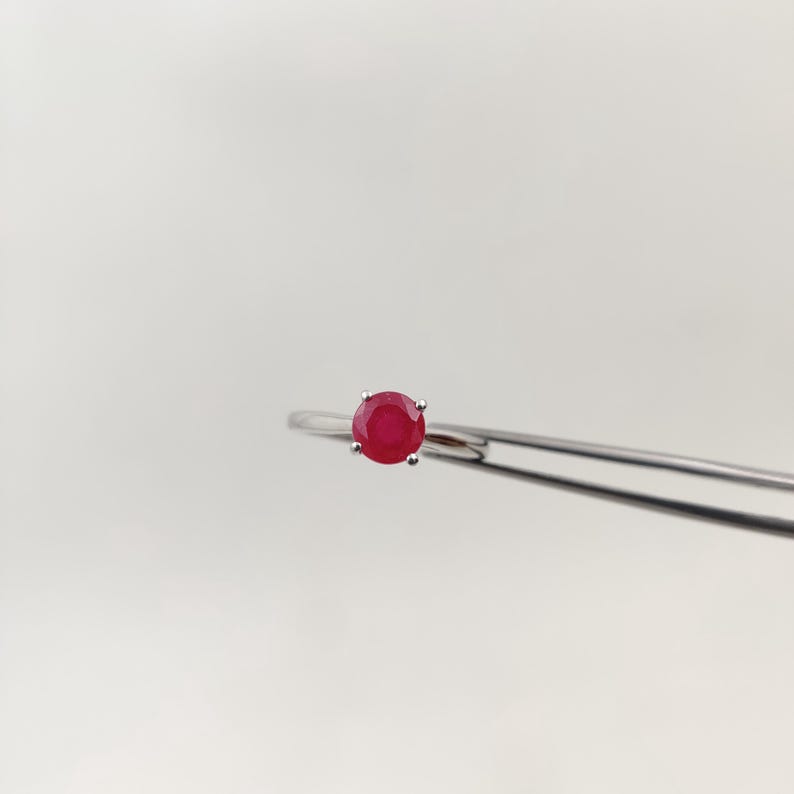 Puede incluir: Un anillo de plata con una gema roja vibrante y redonda. El anillo tiene una banda delgada y delicada, con la gema sujeta por cuatro peque&ntilde;as garras. El anillo se muestra sobre un fondo blanco liso.