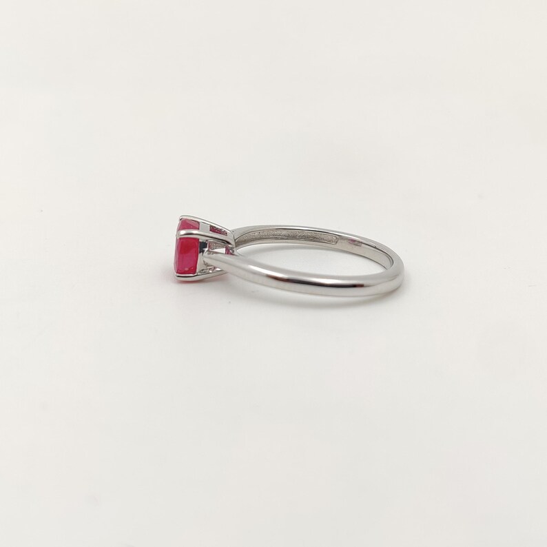 Puede incluir: Un anillo de plata con una llamativa gema roja. El anillo tiene una banda de plata pulida y la gema es de corte cuadrado. El anillo se muestra sobre un fondo blanco liso, resaltando su elegante dise&ntilde;o.