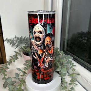 May include: A stainless steel tumbler with a horror movie theme. The tumbler has a black background with the word "Terrifier" in red. The design includes a clown and a woman with a gag. The word "Circus" is also visible.