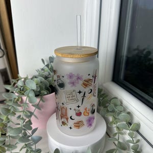 K&ouml;nnte beinhalten: Ein mattierter Glasbecher mit Bambusdeckel und Strohhalm. Der Becher ist mit verschiedenen Stickern im Hexenstil verziert, darunter ein Halbmond, ein Kessel, ein Buch und ein Dolch. Der Text "Ich werde heute nicht sterben" ist auf den Becher gedruckt.