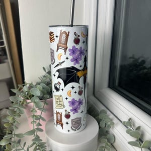 Op de afbeelding: Een witte roestvrijstalen tumbler met een zwart en geel drakenontwerp. De tumbler is versierd met verschillende magische symbolen en illustraties, waaronder een kroon, een flesje drank, een halve maan en een boek. De tekst "Ik zal vandaag niet sterven" is gedrukt op een rol. De tumbler heeft een zwart deksel en een zilveren rietje.