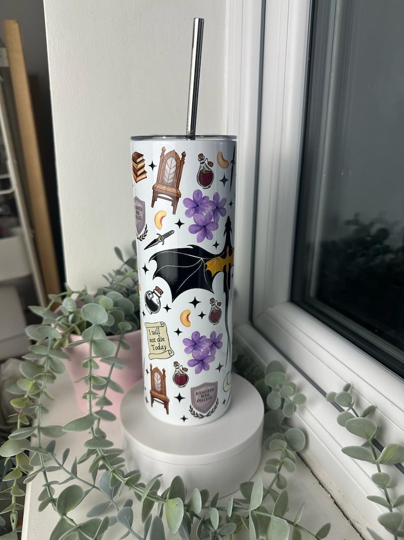 Op de afbeelding: Een witte roestvrijstalen tumbler met een zwart en geel drakenontwerp. De tumbler is versierd met verschillende magische symbolen en illustraties, waaronder een kroon, een flesje drank, een halve maan en een boek. De tekst "Ik zal vandaag niet sterven" is gedrukt op een rol. De tumbler heeft een zwart deksel en een zilveren rietje.