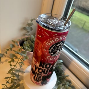 May include: A pink and black stainless steel tumbler with a lid and straw. The tumbler has a graphic of a donut with the words "Ghost" and "Coffee" on it. The tumbler also has the words "No You Hang Up" on it.