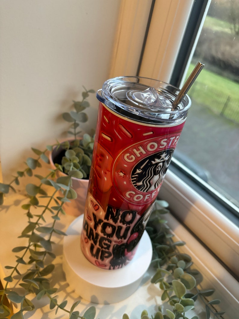 May include: A pink and black stainless steel tumbler with a lid and straw. The tumbler has a graphic of a donut with the words "Ghost" and "Coffee" on it. The tumbler also has the words "No You Hang Up" on it.