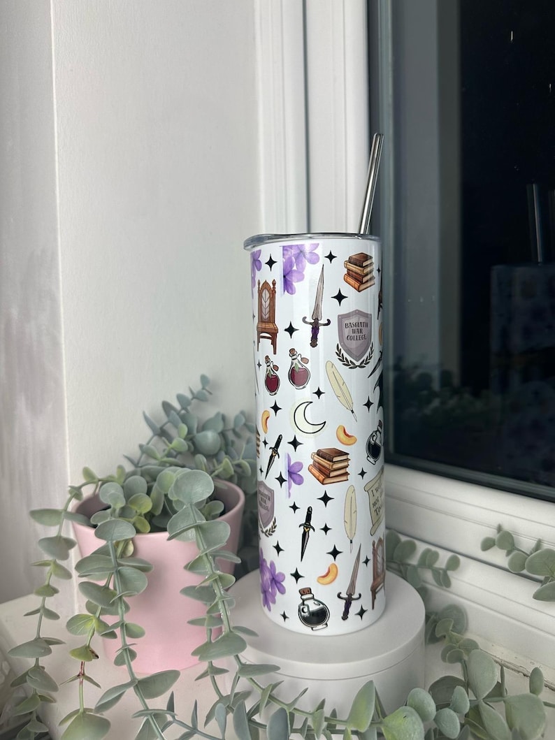 Op de afbeelding: Een witte roestvrijstalen beker met een zwart-wit patroon van verschillende magische voorwerpen, waaronder boeken, veren, drankjes, dolken en een wapenschild met de tekst "Hogwarts School voor Hekserij en Toverkunst".