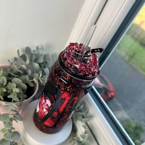 May include: A red glitter tumbler with a clear straw. The tumbler has a black and red design with a portrait and the number 17. The top is filled with red crystals.