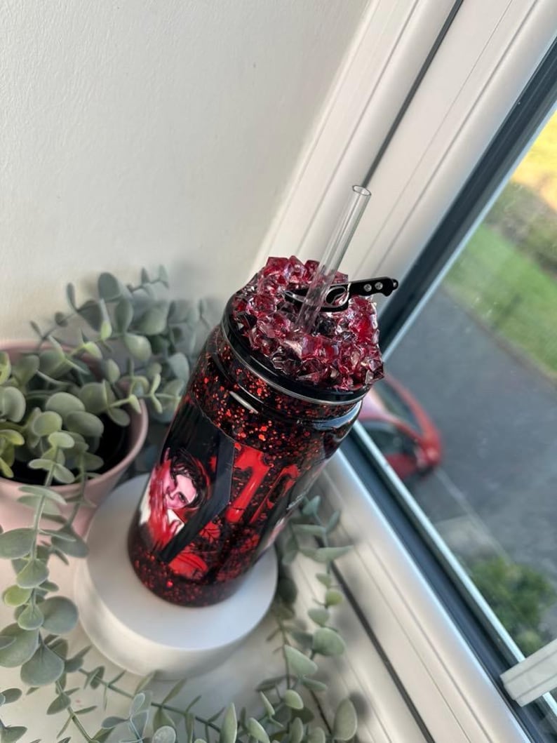 May include: A red glitter tumbler with a clear straw. The tumbler has a black and red design with a portrait and the number 17. The top is filled with red crystals.