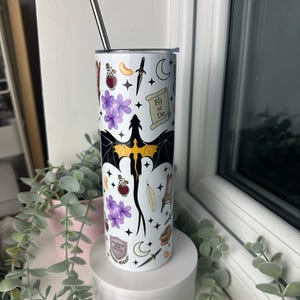 Op de afbeelding: Een witte roestvrijstalen tumbler met een zwarte draak, paarse bloemen en andere magische symbolen. De tumbler heeft de tekst "Fly or Die" erop.