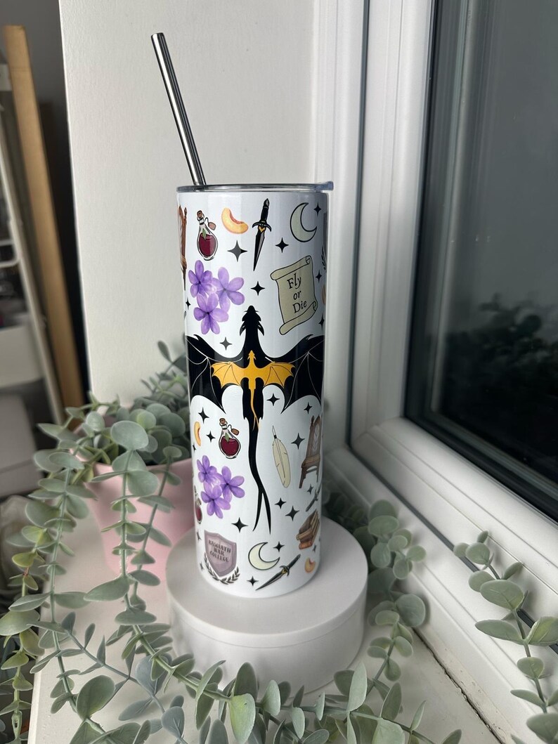 Op de afbeelding: Een witte roestvrijstalen tumbler met een zwarte draak, paarse bloemen en andere magische symbolen. De tumbler heeft de tekst "Fly or Die" erop.