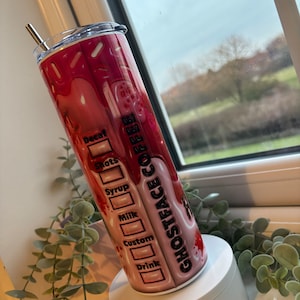 May include: A pink and white stainless steel tumbler with a black and white graphic of a ghost face and the text "Ghostface Coffee". The tumbler has a black lid and a stainless steel straw.