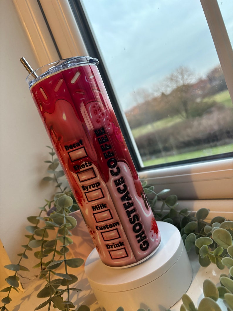 May include: A pink and white stainless steel tumbler with a black and white graphic of a ghost face and the text "Ghostface Coffee". The tumbler has a black lid and a stainless steel straw.