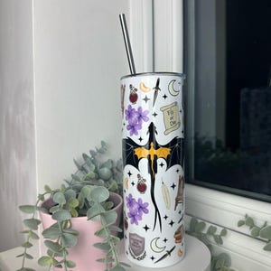 Op de afbeelding: Een witte roestvrijstalen tumbler met een zwart en geel drakenontwerp. De tumbler is bedekt met verschillende stickers, waaronder een halve maan, een veer, een flesje met een toverdrank, een dolk en een rol die "Fly or Die" zegt.