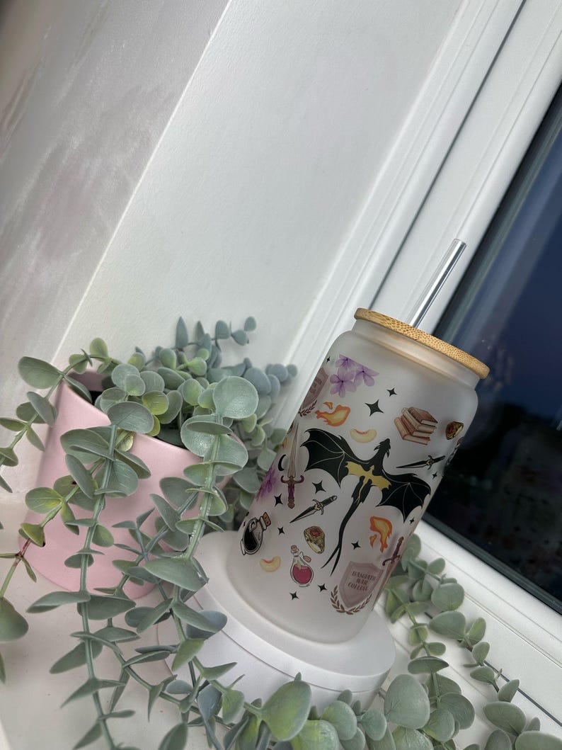 K&ouml;nnte beinhalten: Ein mattierter Glasbecher mit Bambusdeckel und einem klaren Strohhalm. Der Becher ist mit einem schwarzen Drachen, Sternen und verschiedenen anderen Fantasy-Motiven verziert. Der Text "Always be kind to witches" ist auf den Becher gedruckt.