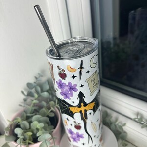 Op de afbeelding: Een witte roestvrijstalen tumbler met een zwarte draak en verschillende magische symbolen, waaronder een flesje met een toverdrank, een dolk, een halve maan en een rol met de tekst "Fly or Die".