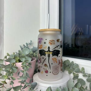 K&ouml;nnte beinhalten: Ein mattierter Glasbecher mit einem schwarzen Drachen und anderen Fantasy-Motiven. Der Becher hat einen Bambusdeckel und einen Strohhalm. Der Text auf dem Becher lautet "Brewed with Magic Coffee".