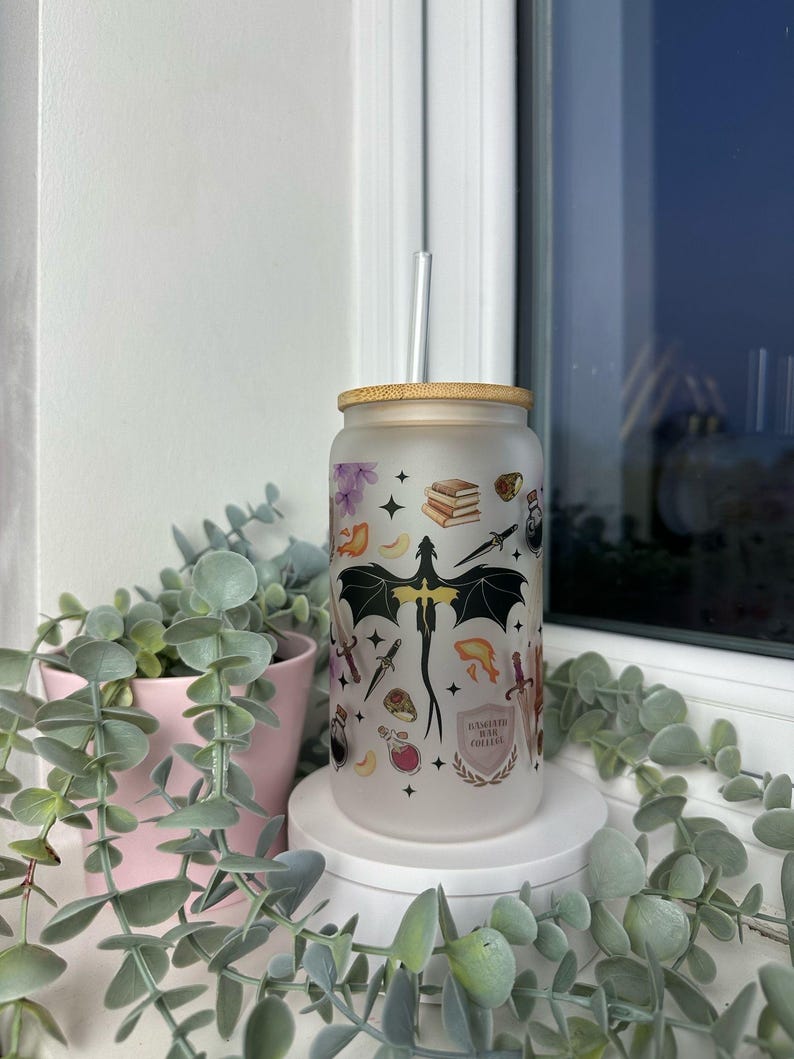 K&ouml;nnte beinhalten: Ein mattierter Glasbecher mit einem schwarzen Drachen und anderen Fantasy-Motiven. Der Becher hat einen Bambusdeckel und einen Strohhalm. Der Text auf dem Becher lautet "Brewed with Magic Coffee".