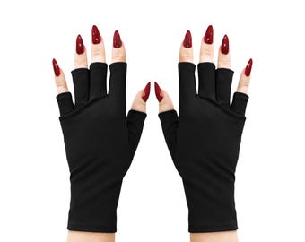 Puede incluir: Un par de guantes negros sin dedos que cubren la palma y el dorso de la mano dejando los dedos expuestos. Los guantes presentan una confección de tela negra lisa y sólida que se extiende desde la muñeca hasta la base de los dedos.
