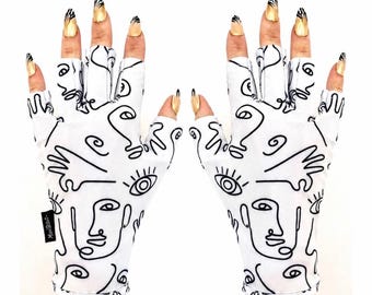 Puede incluir: Un par de guantes blancos sin dedos con un patrón de líneas negras continuas de rostros, ojos y manos abstractos. Los guantes tienen una pequeña etiqueta de tela negra en el lateral con el texto ManiGlovz impreso en color blanco.