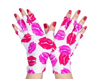 Puede incluir: Guantes sin dedos con una base de color blanco y un patrón repetitivo de marcas de besos de lápiz labial en color rosa vibrante. Los guantes cubren la palma y el dorso de la mano, dejando los dedos expuestos, con un ajuste ceñido y flexible.